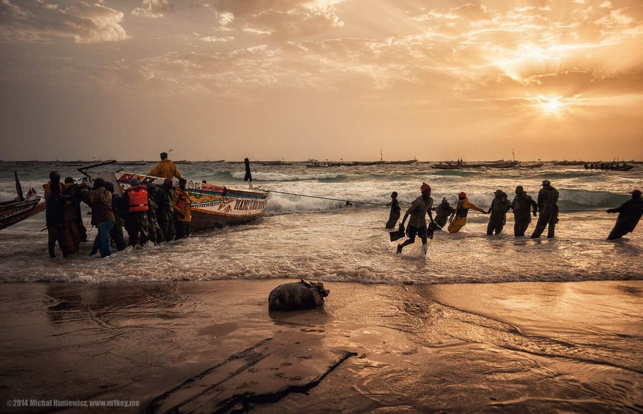 Fishermen hold a boat, which is temporarily anchored to the shore, to remove fish at sunset off the coast of Mauritania.