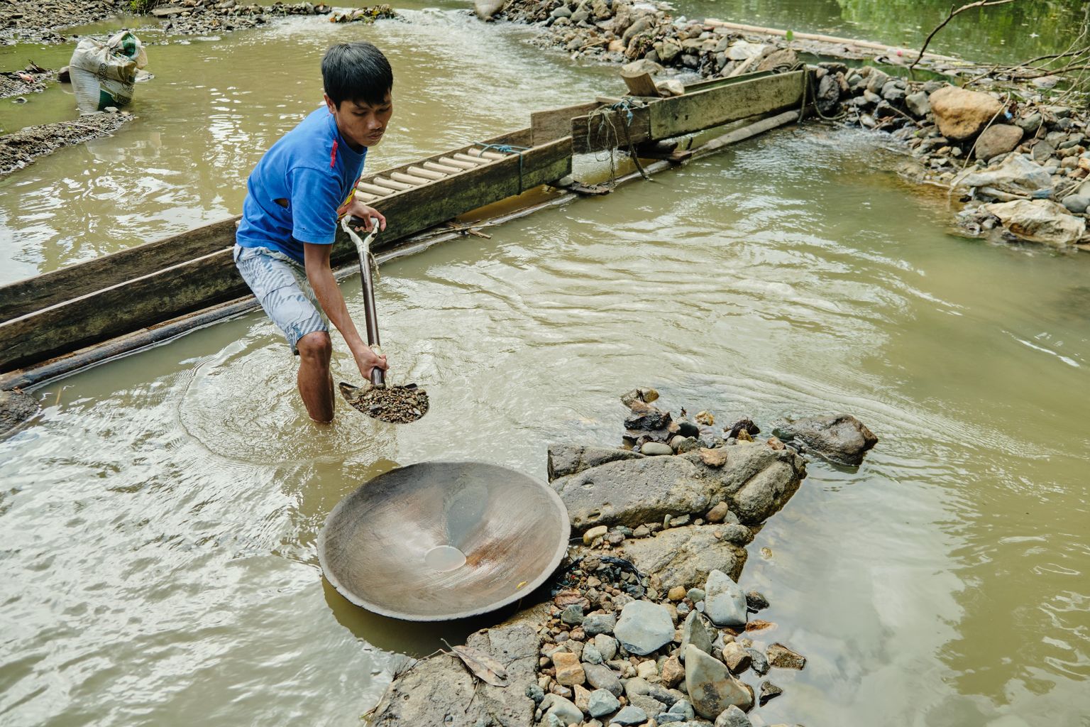 Eron shovels ore from the riverbed into the gold pan.